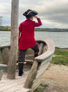 back of a child wearing red and black pirate captain costume looking out over water.