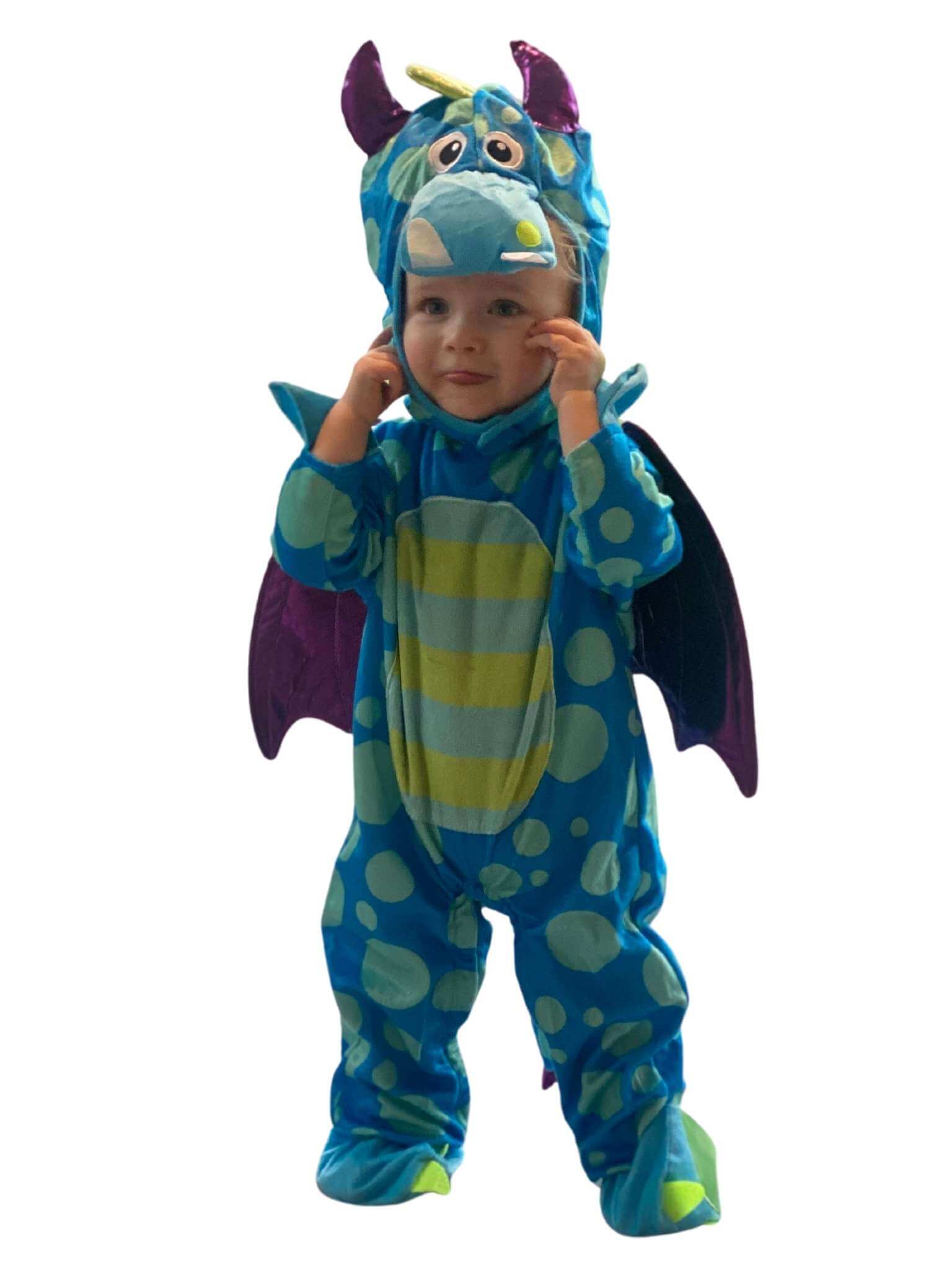 Toddler wearing blue and green spotty dragon costume sticking their tongue out. 