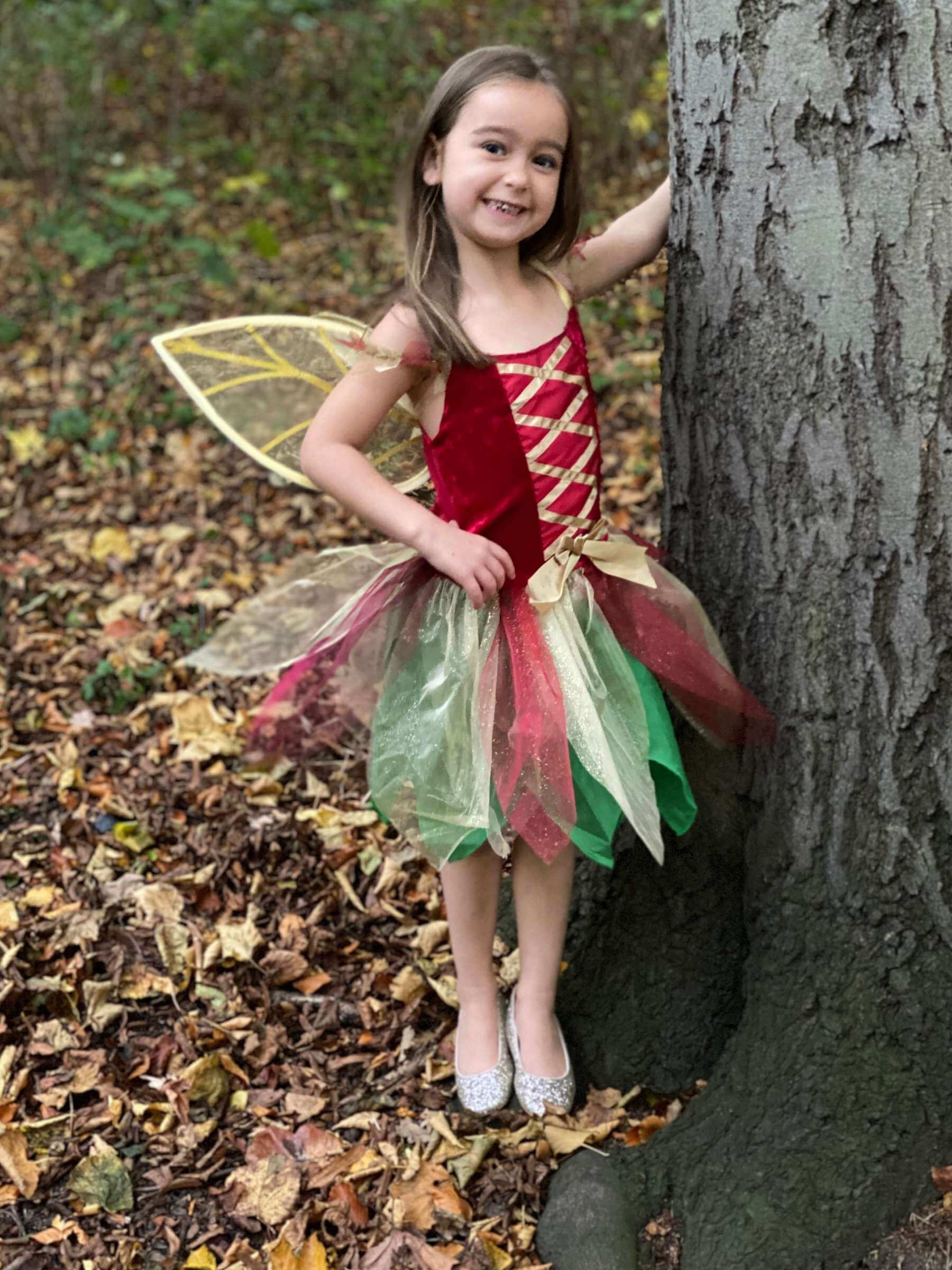 Girl standing next to a tree showing the red gold and green fairy dress costume.