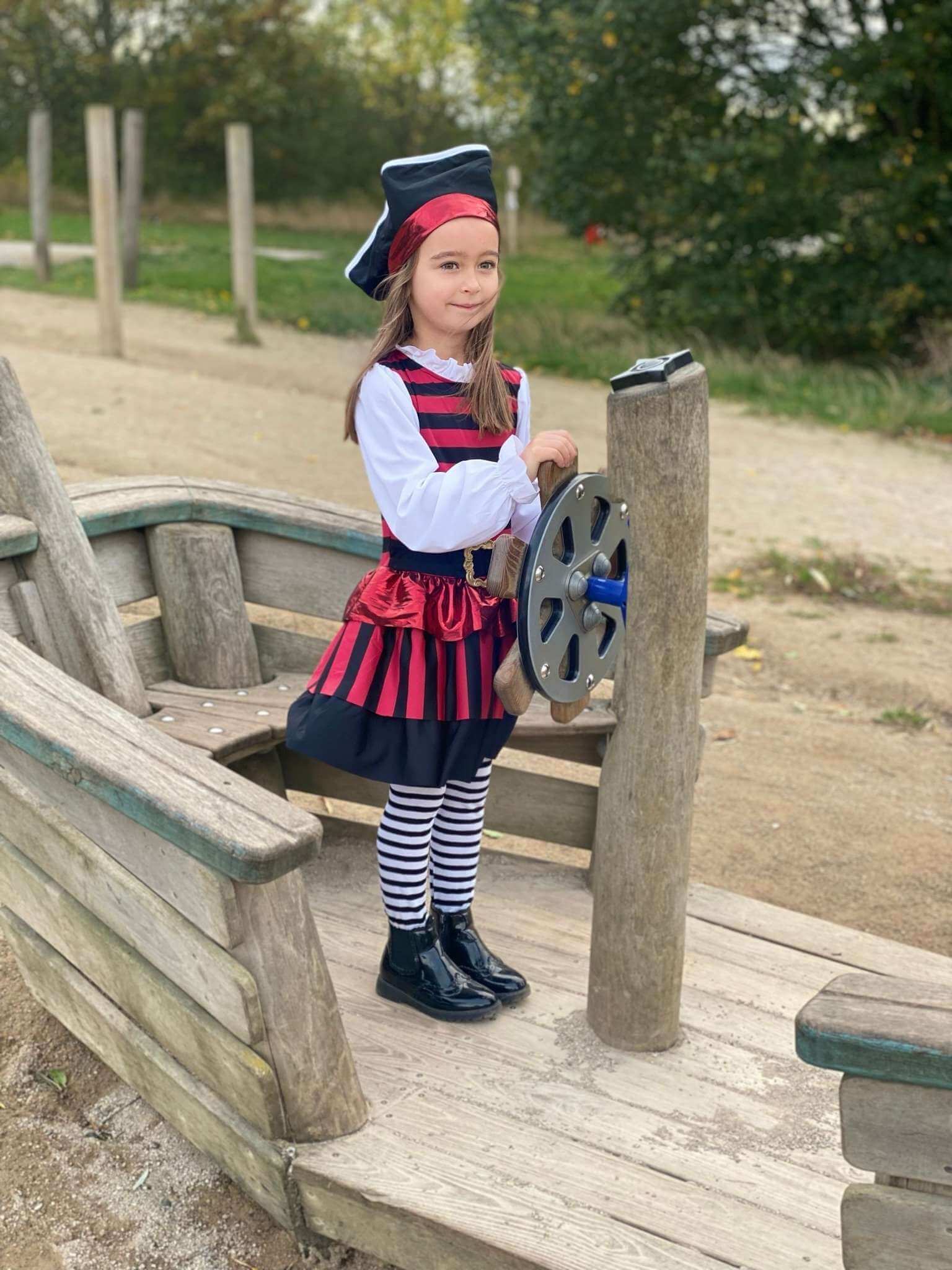 A girl stood on a wooden boat wearing the pirate costume.