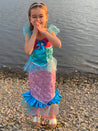 Girl stood next to water laughing wearing the blue and pink mermaid dress.