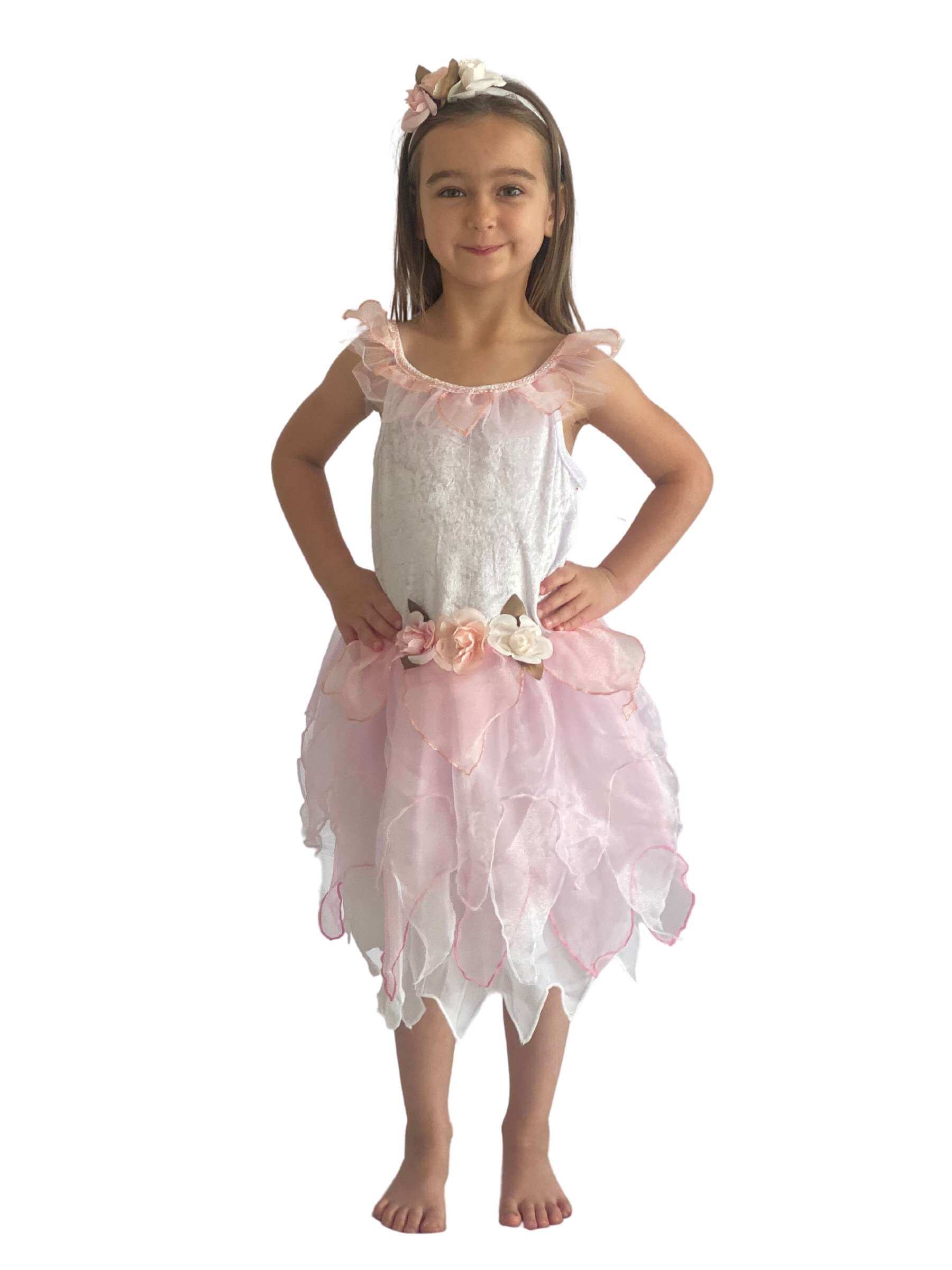 Girl with her hands on her hips wearing a white fairy costume with pink layered skirt, flower detail to the wait and a headband with flowers on.