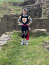Boy stood in front of castle ruins wearing the Knight costume with his hands on his hips.