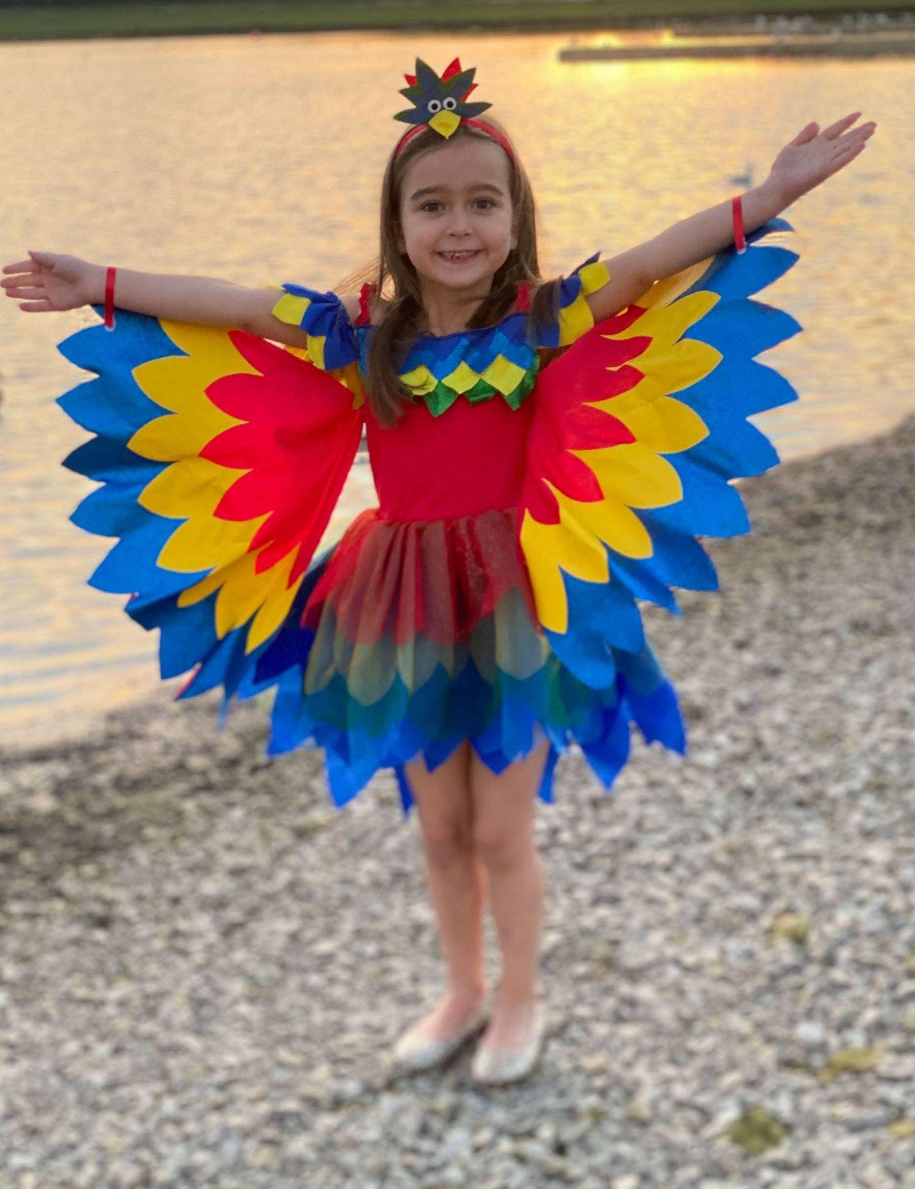Girl stood in front of water wearing red yellow and blue macaw parrot costume.