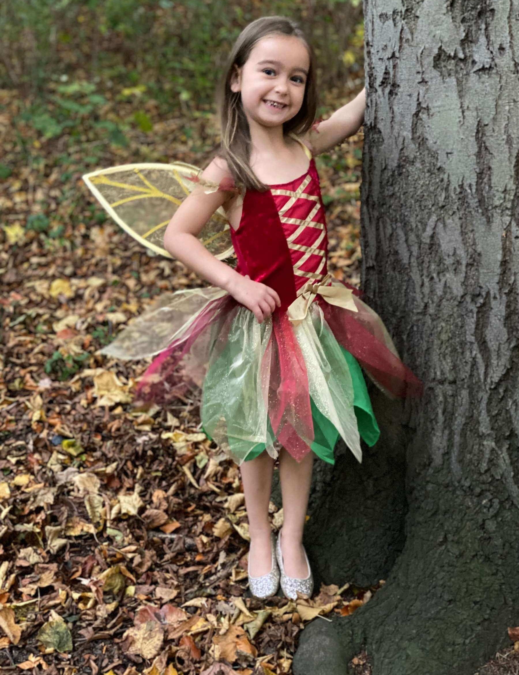 Girl standing next to a tree showing the red gold and green fairy dress costume.