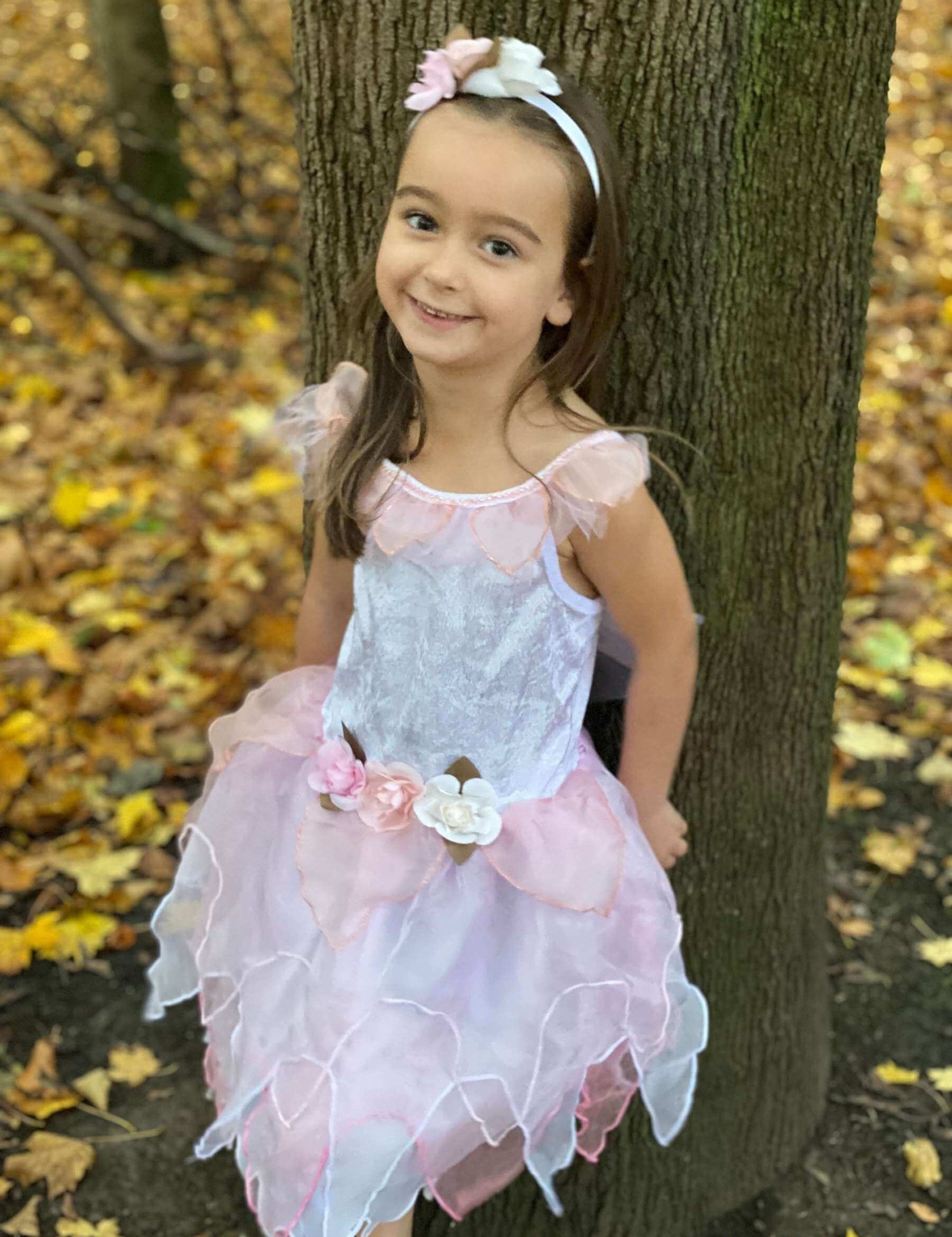 Girl leaning against a tree wearing the white and pink fairy dress.