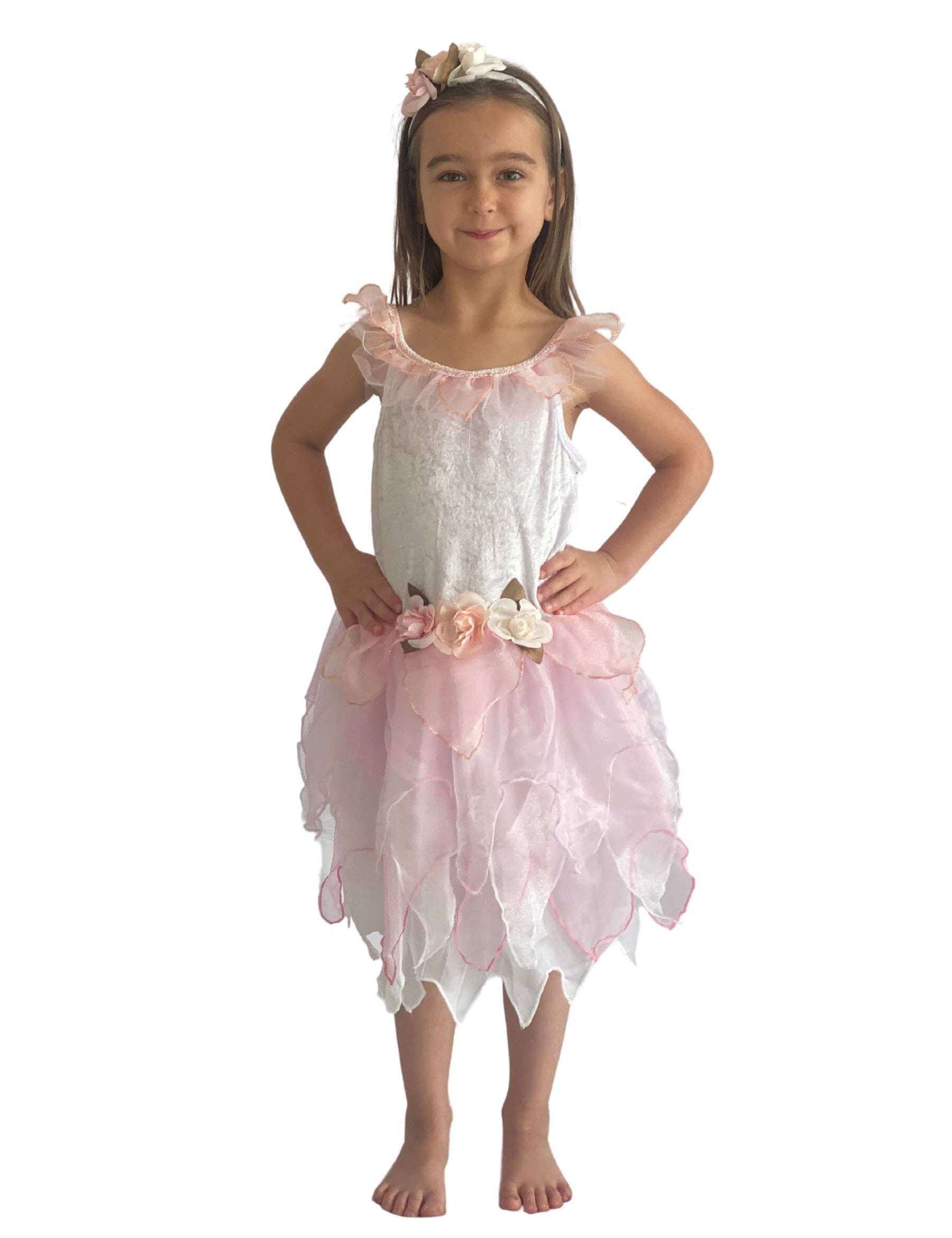 Girl with her hands on her hips wearing a white fairy costume with pink layered skirt, flower detail to the wait and a headband with flowers on.