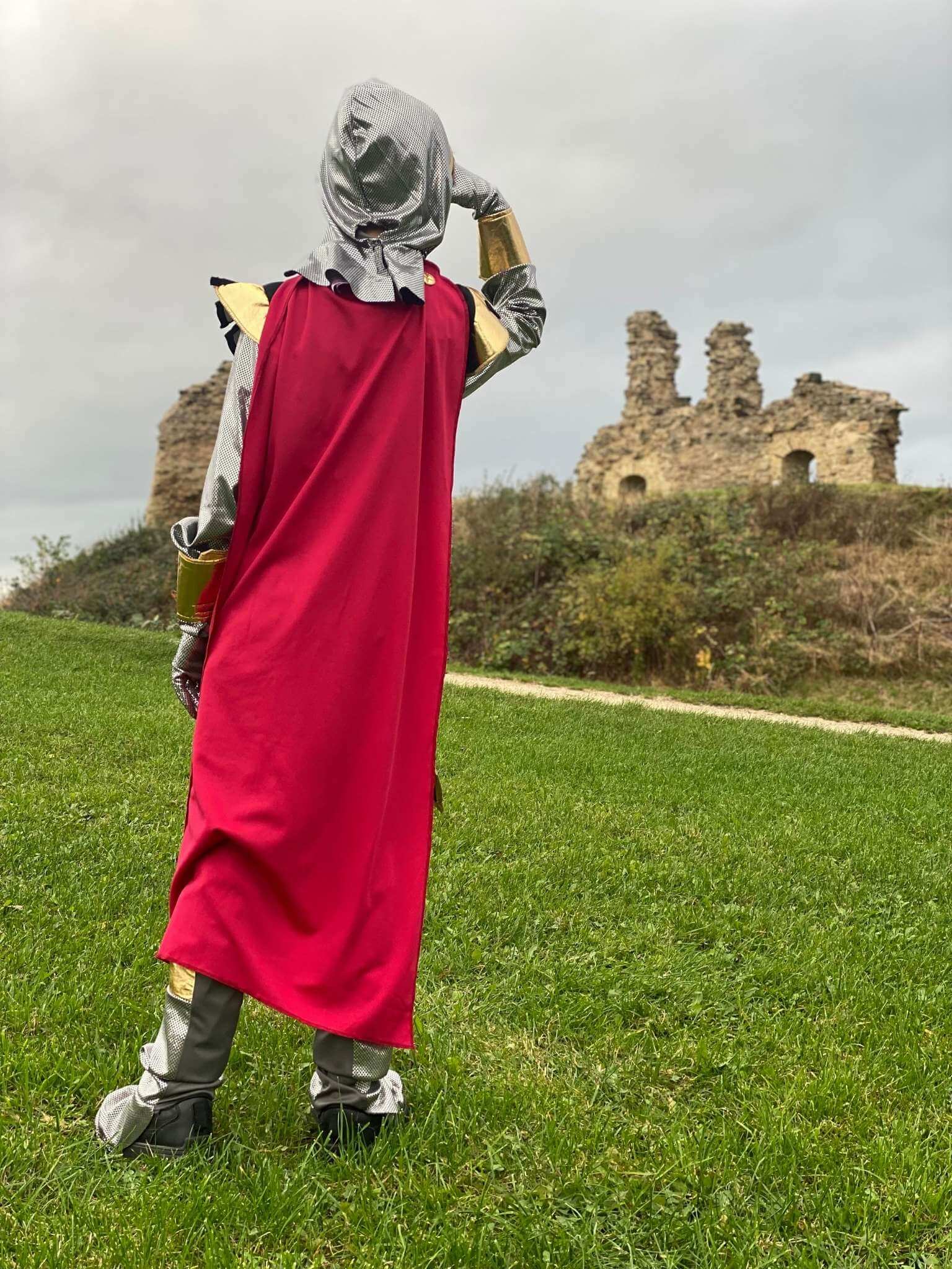 Back of the boy looking into the distance at the castle ruins showing the red cape.